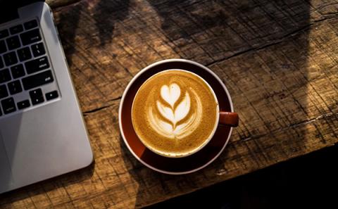 Cappuccino ja läppärin kulma puisella pöydällä. Kuva Nolan Issac, Unsplash.com